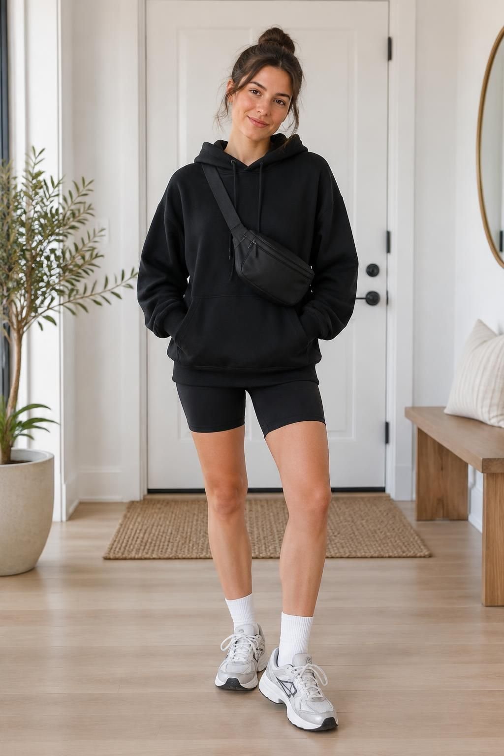 A roomy black hoodie worn with black biker shorts, crew socks, sneakers, and a belt bag.