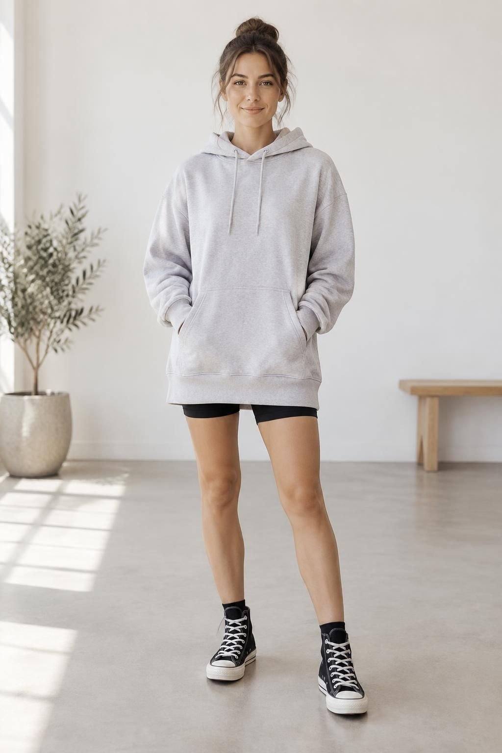 Long pale-grey hoodie with a narrow strip of black biker shorts and high-top sneakers.