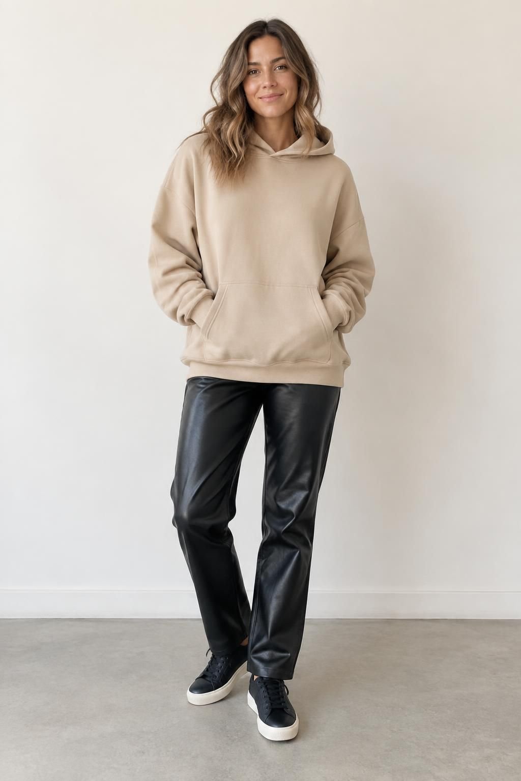 Plain sand hoodie with smooth black leather-look trousers and black sneakers.